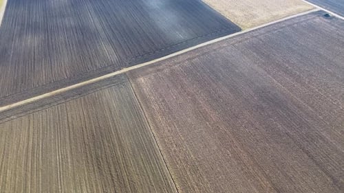 Vue aérienne par drone de vastes terres agricoles labourées avec des motifs géométriques de champs, mettant en valeur des terres agricoles