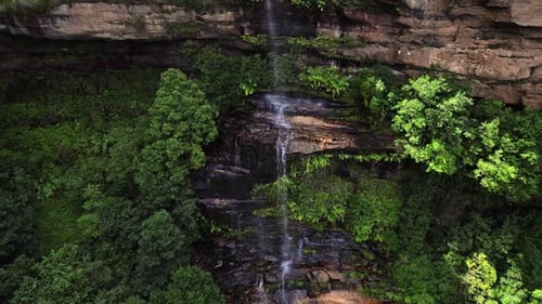 A Beautiful Waterfall Cascades Down a Rugged Rock Face Surrounded By Lush Green Vegetation Mist
