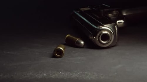 Bullets drop near handgun on table and roll away, slow motion