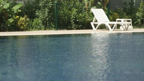 Ein Blick auf das blaue Wasser des Pools und ein weißer Liegestuhl vor dem Hintergrund von Büschen