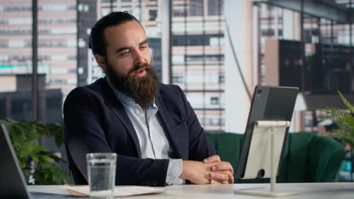 Bearded Man Video Conferencing on Tablet in Office