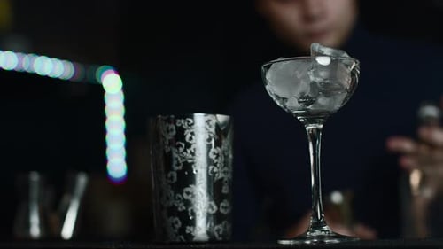 Close up of glass with ice cubes prepared for cocktail. Media. Bartender mixing alcohol liquids