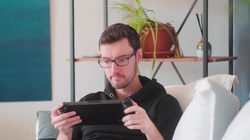 Young Adult Playing Handheld Gaming Console at Home