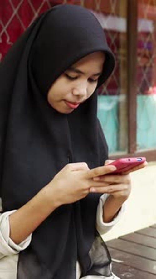 Young Asian Muslim Girl Using Smart Phone Device at Street