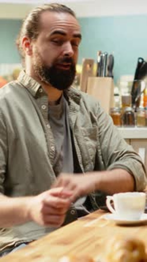 Man Talks Over Laptop at Kitchen Table Indoors
