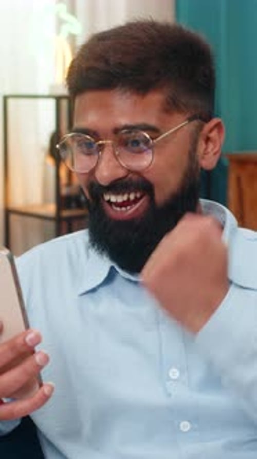 Man Celebrates Success on Smartphone Indoors