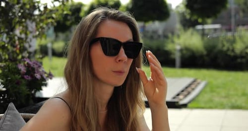 Entspannte Frau mit langen Haaren passt ihre Sonnenbrille im Sunny Park an