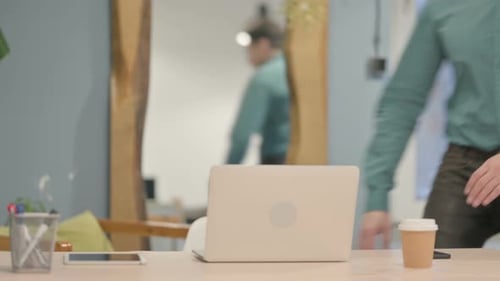 Man Walks to Desk and Works on Laptop