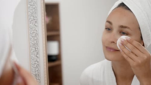 Woman Cleansing Face with Cotton Pad in Bathroom