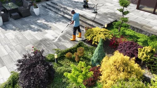 Gardener Using a Pressure Washer to Clean Stone Path in Beautifully Landscaped Garden