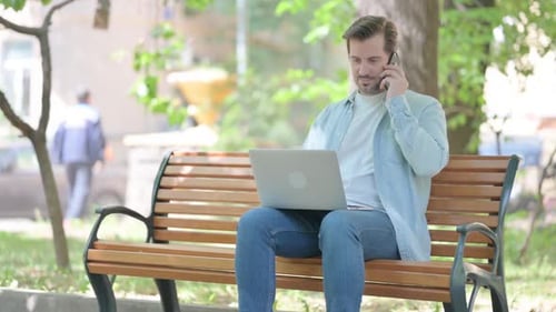 Man Works on Laptop and Phone in Park