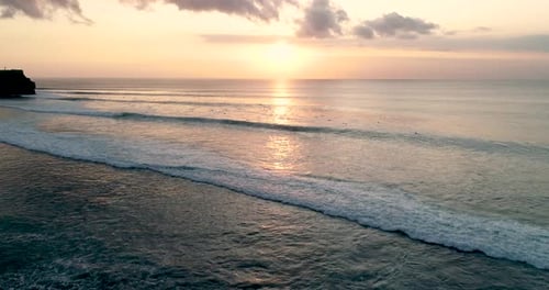Aerial Shot Fly Over Blue Ocean And Tropical Beach Cloudy Sunset Dawn with many surfers view at Bali