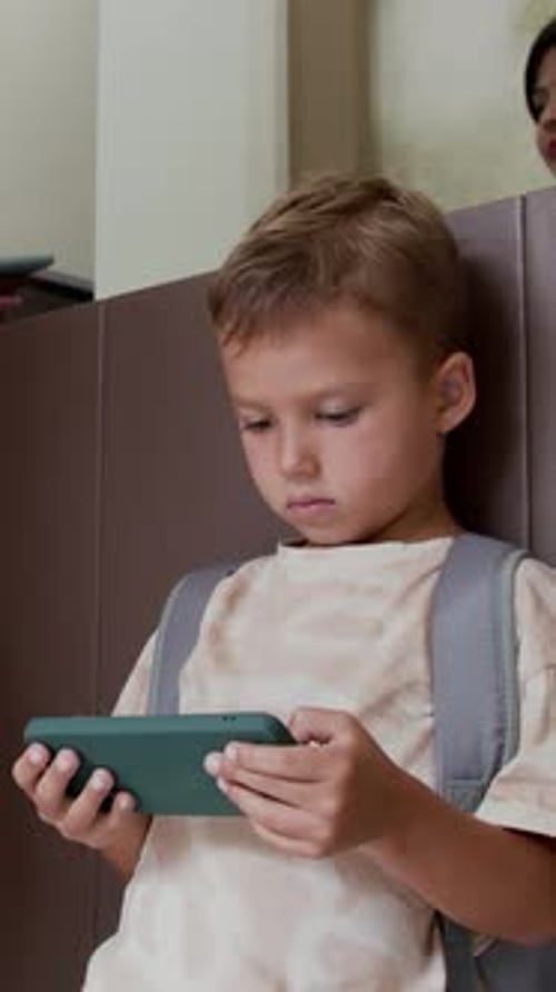 Boy Playing Phone while Parents Checking In at Hotel Reception