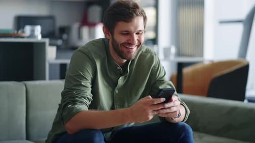 Man Smiling Using Smartphone on Couch Indoors
