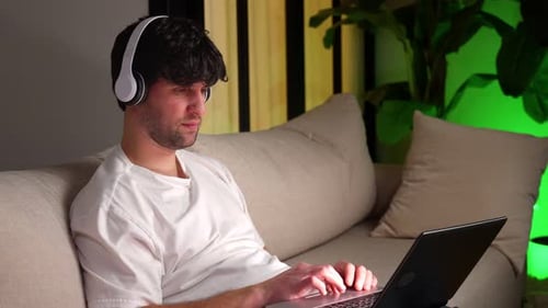 Young Adult Using Laptop with Headphones on Sofa