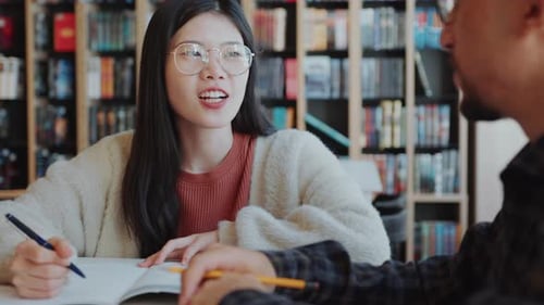 Asian Girl Smiling and Discussing Homework with Group Mate in Library