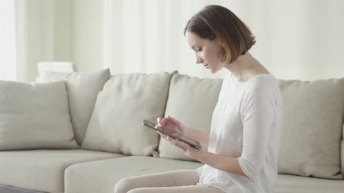 Woman Using Tablet on Couch in Bright Home