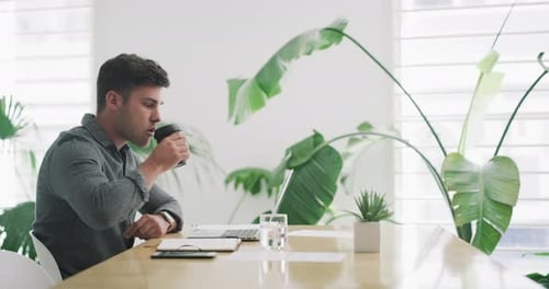 4k-Videomaterial eines jungen Geschäftsmannes, der Kaffee trinkt und in einem Büro an einem Laptop arbeitet