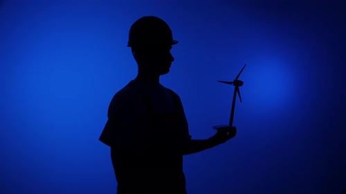Engineer Silhouette Wearing a Hard Hat Holding a Miniature Wind Turbine Model in Hand Representing