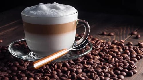 Tasse mit heißem Cappuccino-Getränk auf gerösteten Kaffeebohnen. dolly shot