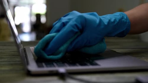 Gloved Hand Cleaning Laptop Keyboard With Cloth