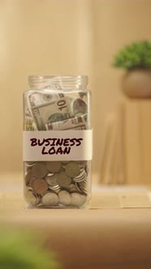 Money Being Placed in Business Loan Jar