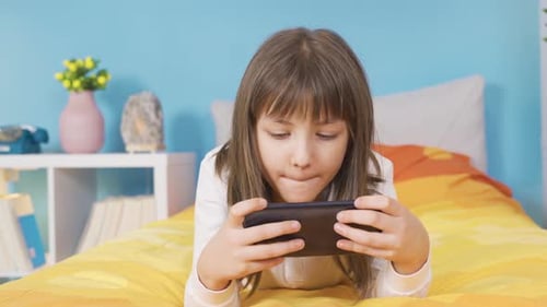 Girl Plays Phone Lying on Bed Indoors