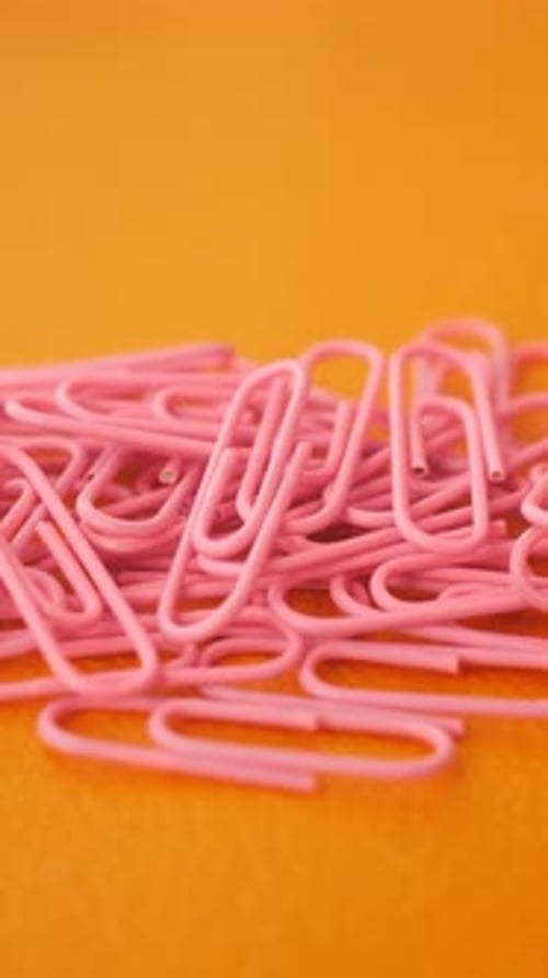 Pink Paperclips Scattered on Bright Orange Surface