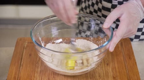 Egg being added to ingredients in glass bowl