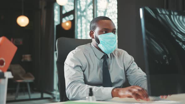 African American Man Wearing Mask Uses Computer for Work in Modern ...