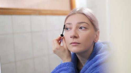 Young Attractive Woman Applying Mascara in Front of Mirror in Bathroom