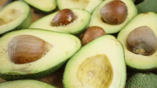 Numerous avocado halves with pits have taken over the entire space on the table. Dolly slider.
