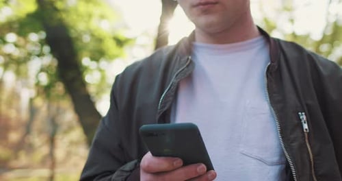 Close Up of Caucasian Young Man Texting and Tapping on Smartphone Device and Putting It in Pocket In