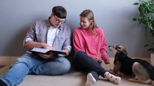 Mujer joven feliz y hombre sentados en la alfombra en casa viendo el álbum de fotos