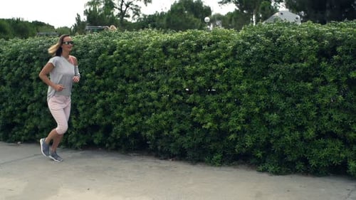 Young woman jogging on pavement in city park super slow motion