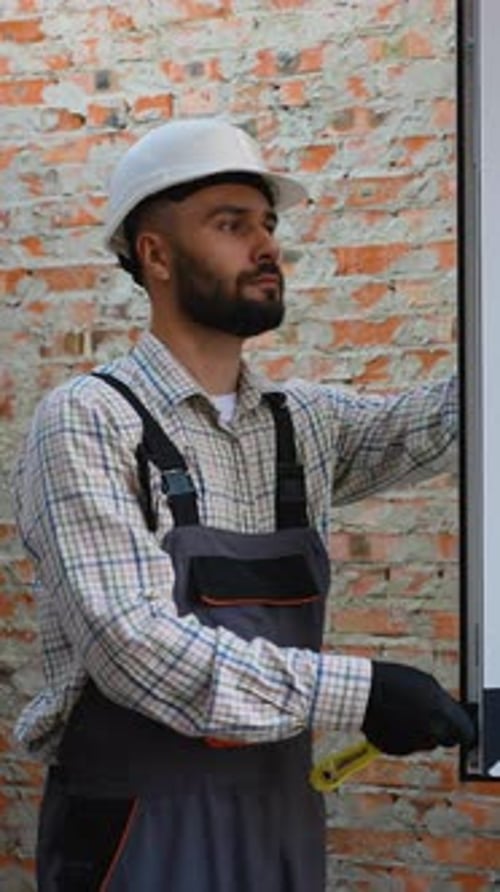 Construction Worker Measuring with Tool in front Brick Wall