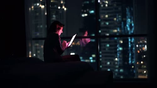 Woman Using Tablet at Night with City View