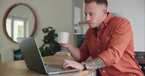 Man Drinks Coffee While Working on Laptop at Home