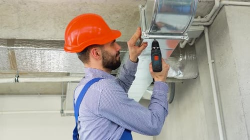 Man Installing Metal Ductwork With Power Drill
