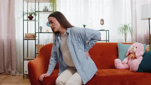 Upset Ill Young Pregnant Woman Feeling Sick Suffering From Lower Back Pain Sitting on Home Sofa