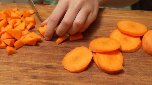 Hands chopping carrots on wooden cutting board