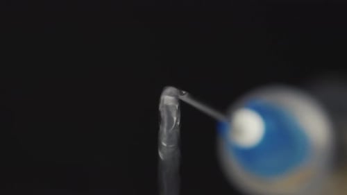 A medical syringe with a vaccine dripping from a needle. Reflection in a drop. Close-up.