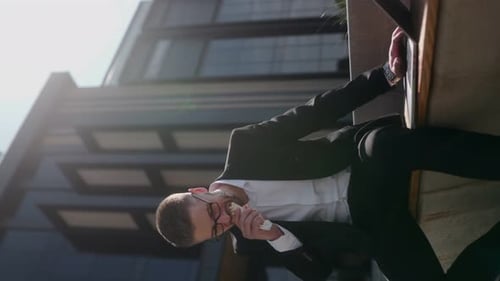 Man in Business Suit Typing on Laptop and Eating Lunch in Front of Office Building