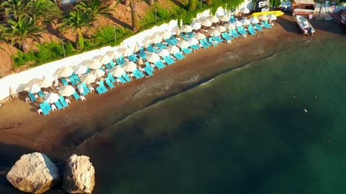 Drone aerial shot of waves hitting the beach full of umbrellas and sunbeds. no human. 4K.