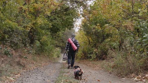 Young Man Goes In Forest With Cute Dachshund Both Wearing Casual Back View