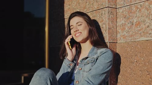 Attractive Young Woman Using Her Smartphone for Conversation with Her Friend While Walking in City