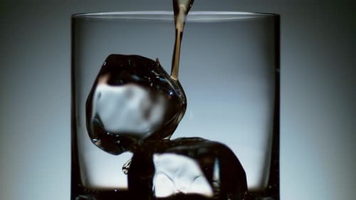 Pouring Dark Liquid Over Ice in Glass