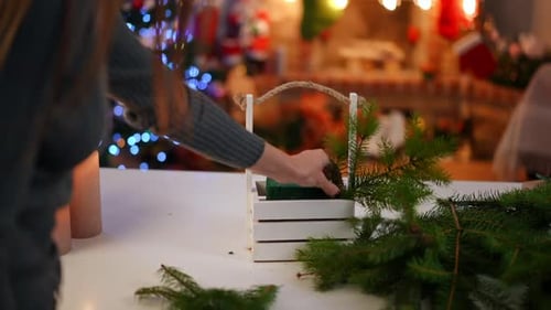 Unrecognizable Woman Putting Green Fir Tree Branches in White Decorative Basket with Christmas