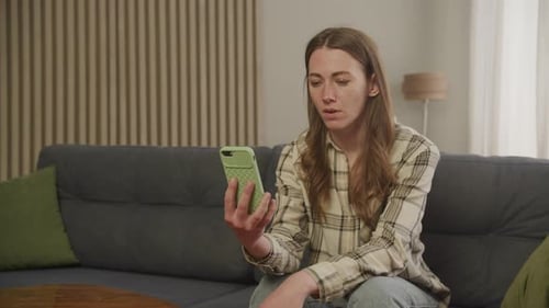 Woman Looking Worriedly at Smartphone in Living Room