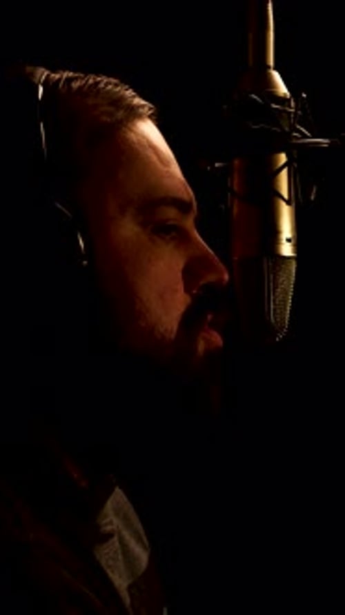 Vertical: Man With Headphones Talking in Front of Professional Microphone in Dark Studio